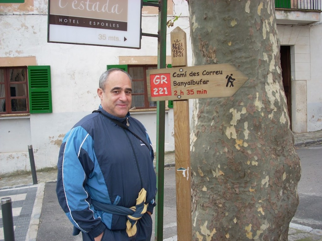 Persona de pie junto a un cartel que indica la dirección del 'Camí des Correu Banyalbufar' en Esporles, Mallorca.