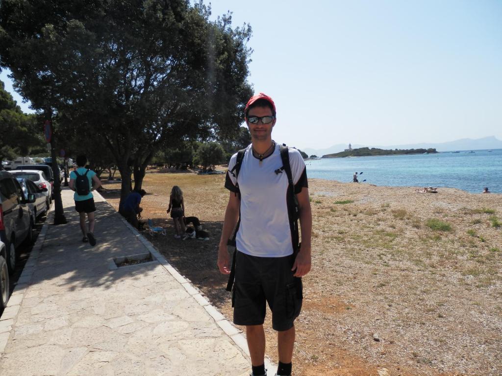 Hombre de pie en un sendero junto a la playa de Alcanada, con vistas al mar y la isla de Alcanada en el fondo.