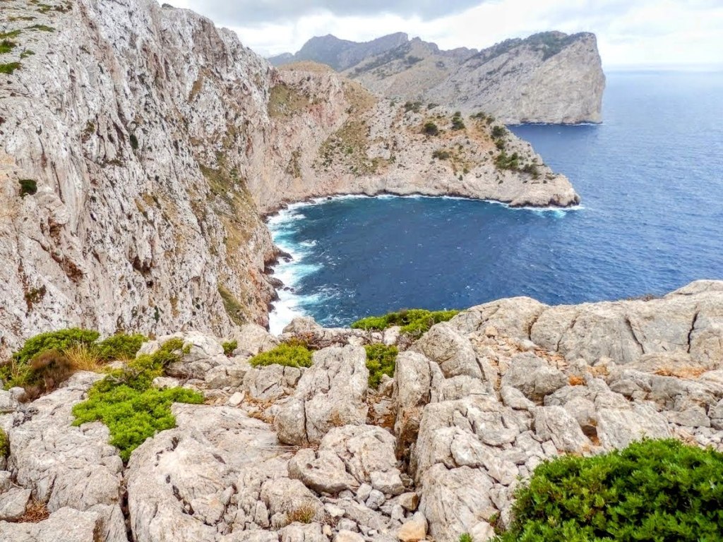 Vista panorámica de la costa de Formentor, mostrando acantilados y una cala con aguas azules, rodeada de formaciones rocosas y vegetación.