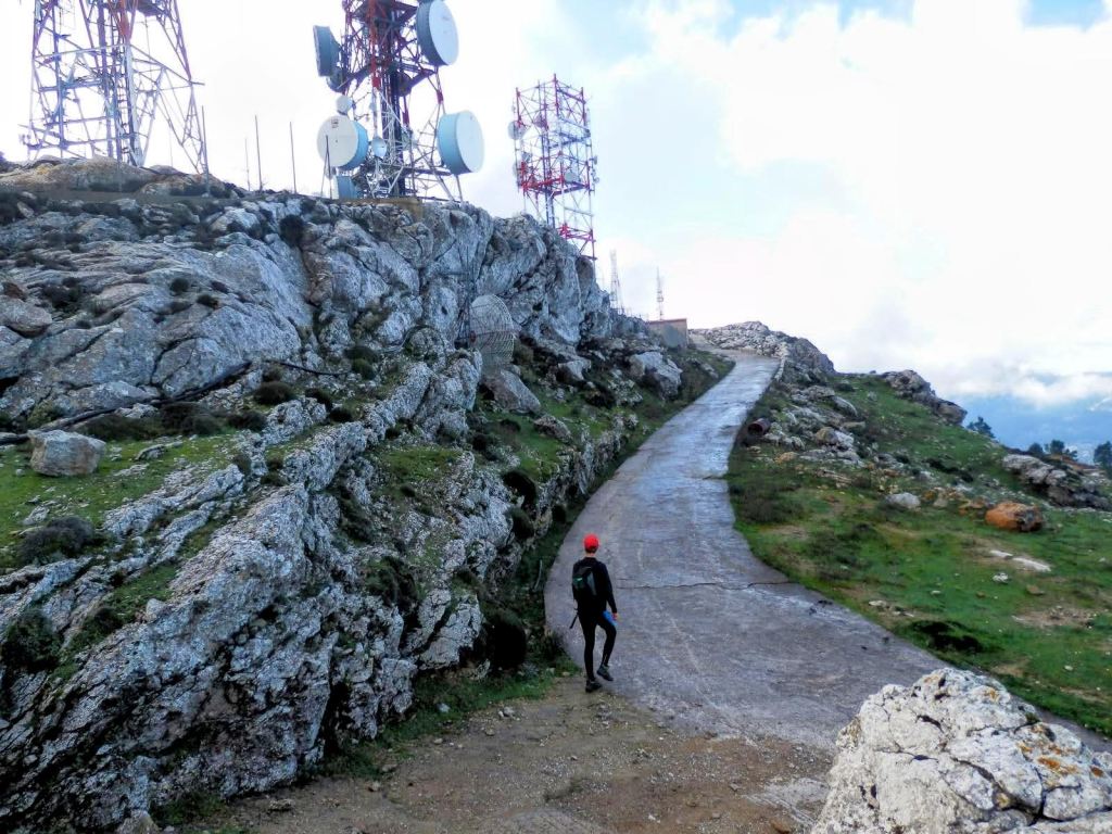 Vista del camino en la Sierra de Alfàbia, rodeado de antenas de telecomunicaciones y rocas, con una persona caminando por la senda.