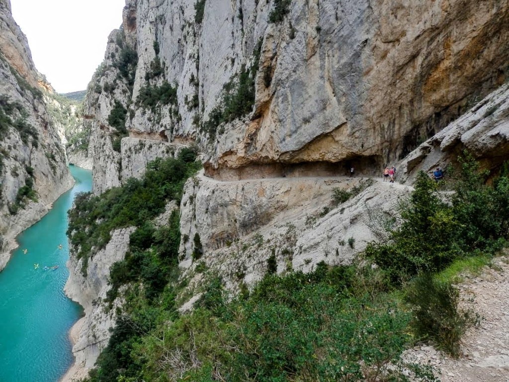 Vista panorámica del Congost de Mont-Rebei, mostrando un sendero excavado en la roca junto a un río de color azul turquesa, rodeado de altas paredes de roca y vegetación.