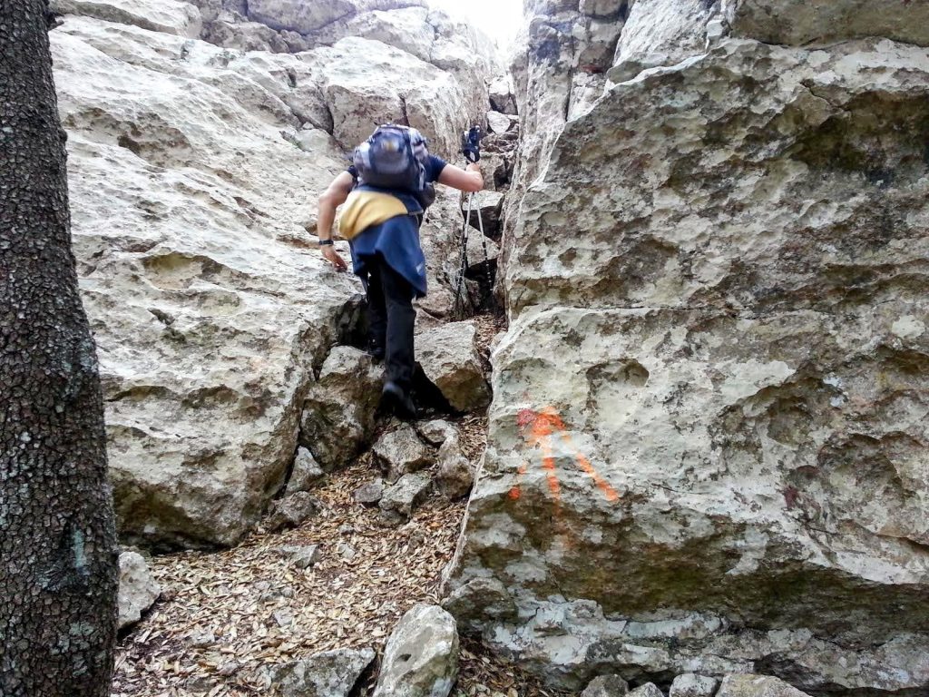 Una persona escalando entre grandes rocas para subir a la Fita del Ram