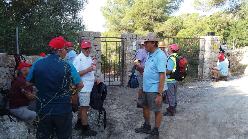 Grupo de personas con gorras rojas conversando cerca de la entrada de la finca Es Fangar, en un camino rural rodeado de vegetación.