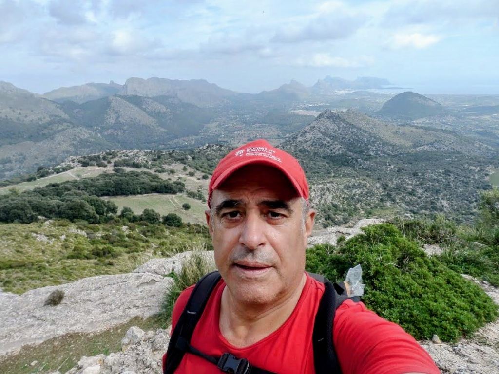 Persona en la cima de una montaña con paisaje montañoso y vistas al fondo.