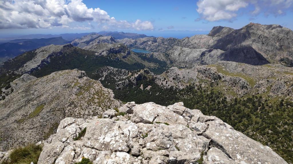Vista panorámica desde la cima del Puig de Massanella, mostrando montañas, vegetación y un embalse en el fondo.