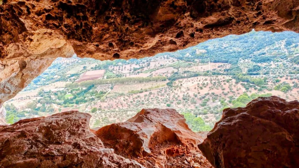 Vista desde el interior de la Cueva de ses Dues Boques, mostrando un paisaje montañoso con campos cultivados y vegetación a lo lejos.