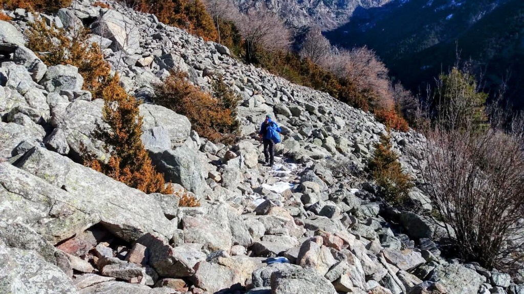 Senderista caminando por la Tartera de Corbel en un paisaje montañoso, rodeado de árboles y montañas al fondo.
