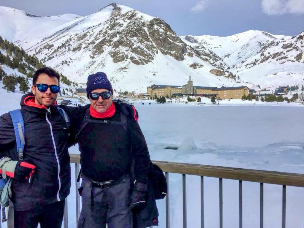 Dos personas posando en un entorno nevado con montañas al fondo, frente al Santuario de Núria en el valle.