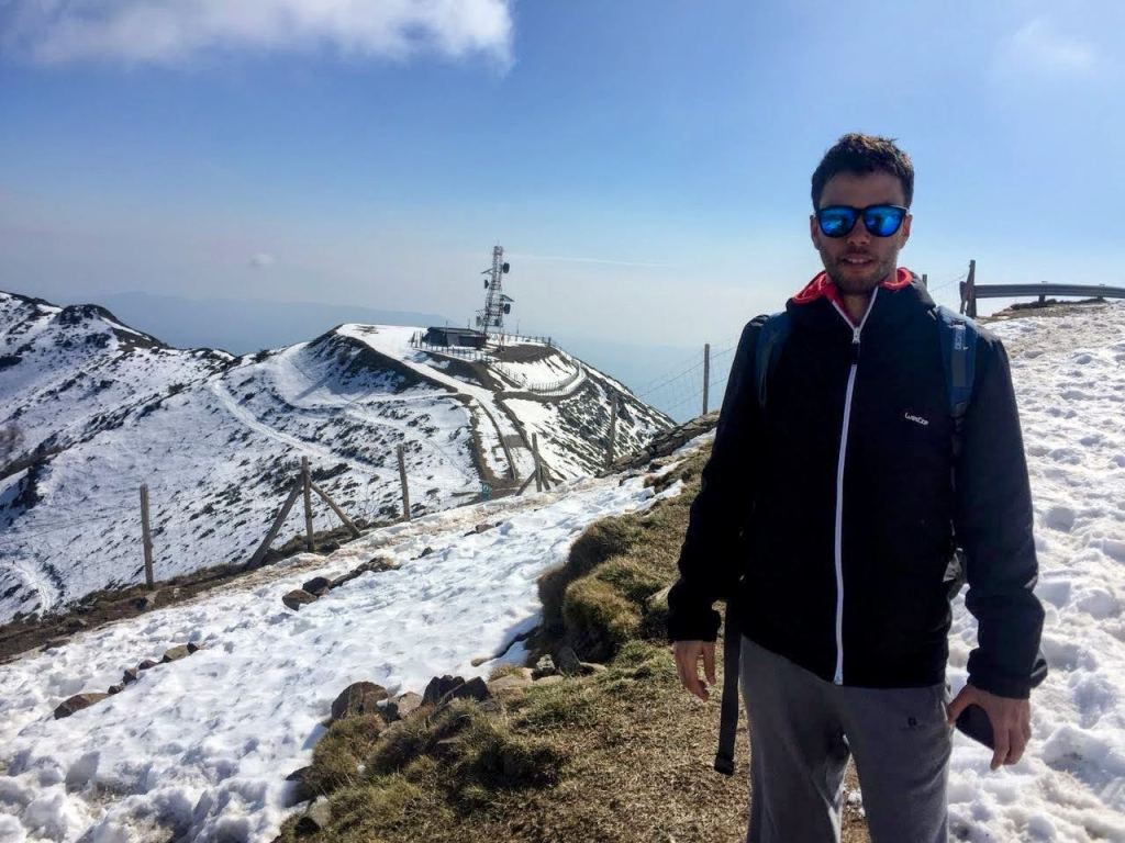 Un senderista de pie en el Turó de l'Home (Monte del hombre) nevado, con un fondo que muestra una cima y una estación de comunicaciones.