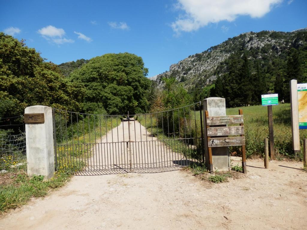 Entrada al sendero hacia El Castellot des Rafal, con una puerta de hierro y señalización al lado, rodeada de vegetación y montañas al fondo.
