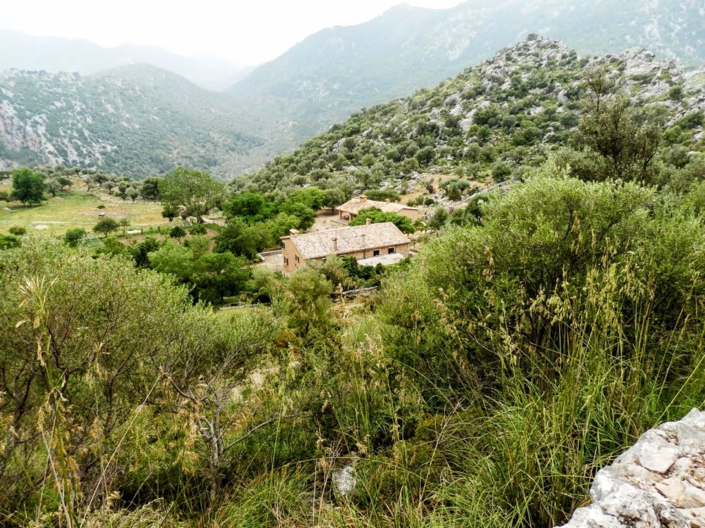 Vista del refugio de Tossal Verds en un paisaje montañoso, rodeado de vegetación y colinas.