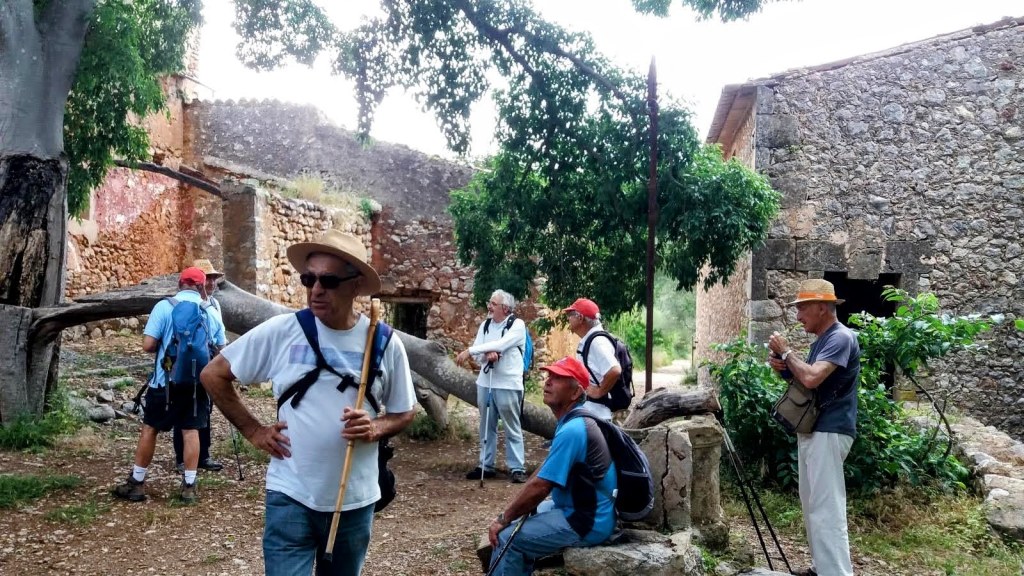 Grupo de senderistas en la antigua posesión de Raixeta, con estructuras en ruinas y vegetación alrededor.