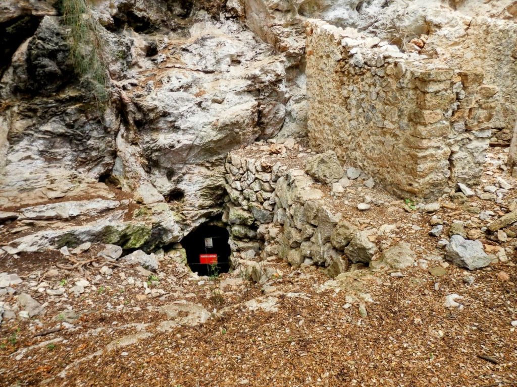 Entrada bloqueada de la Cueva de las Maravillas, con paredes de piedras y un letrero de prohibición de acceso.