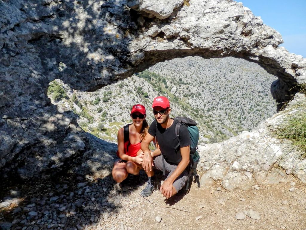 Pareja posando en una formación rocosa con un agujero, con un paisaje montañoso al fondo.