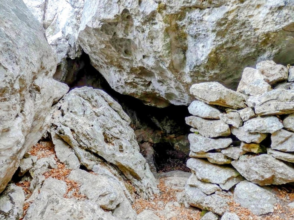 Entrada a la Cova dels Ermassets rodeada de rocas y piedras, con un pequeño muro de piedra a su alrededor.