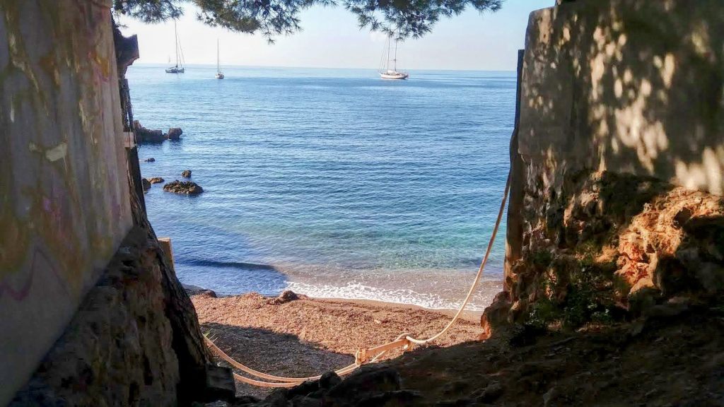 Vista de una cala con agua cristalina y barcos en el horizonte, enmarcada por rocas y vegetación.