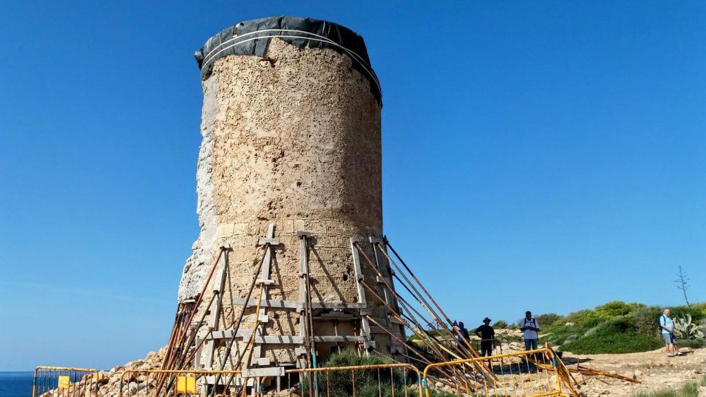 Vista de una torre de vigilancia en proceso de restauración, con andamios de soporte y un cielo despejado al fondo.