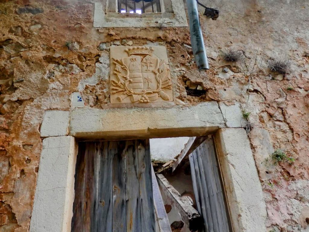 Puerta deteriorada de Raixeta, con un escudo en la parte superior y una estructura de madera visible en su interior.