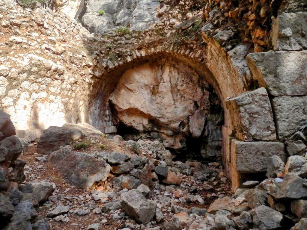 Ruinas de la Font de sa Gruta, con piedras dispersas y un arco de piedra en la parte superior.