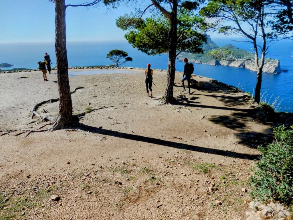 Tres senderistas caminando por la  Era de trillar con vistas al mar, rodeados de pinos en la ruta La Trapa-Torre de Cala en Basset.