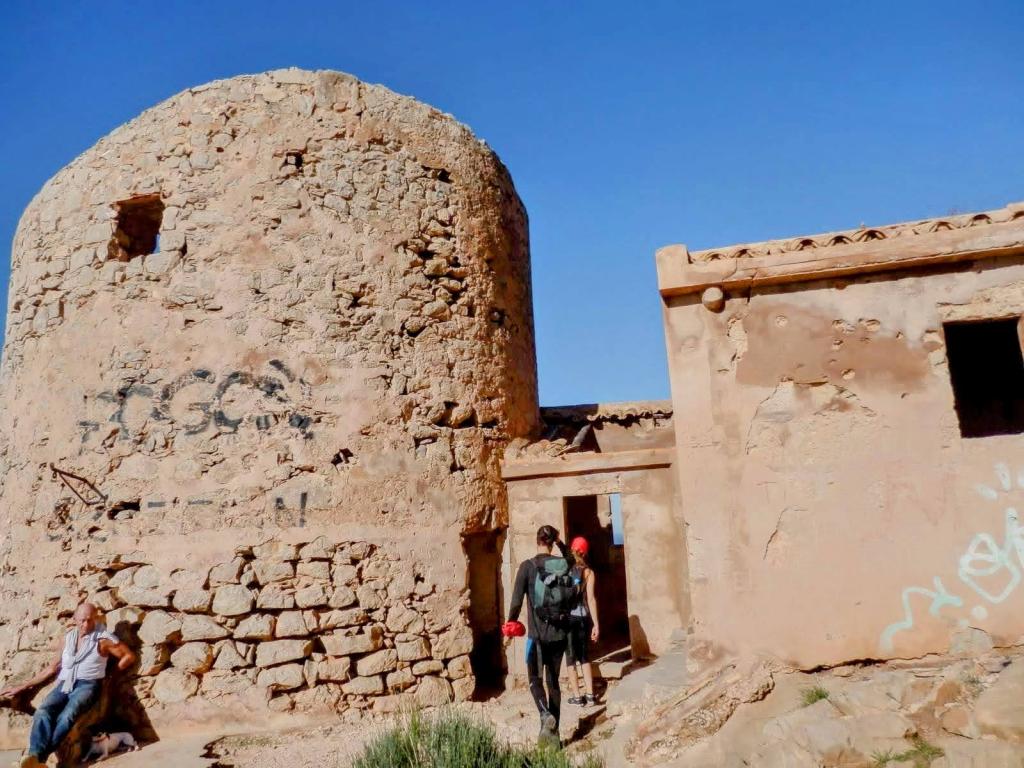 Grupo de senderistas explorando ruinas de un edificio con paredes de piedra y graffiti, bajo un cielo azul.