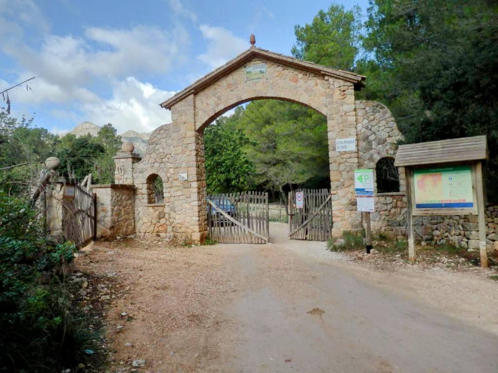 Entrada a la finca pública de Galatzó, con un gran arco de piedra y una puerta de madera, rodeada de vegetación y montañas al fondo.