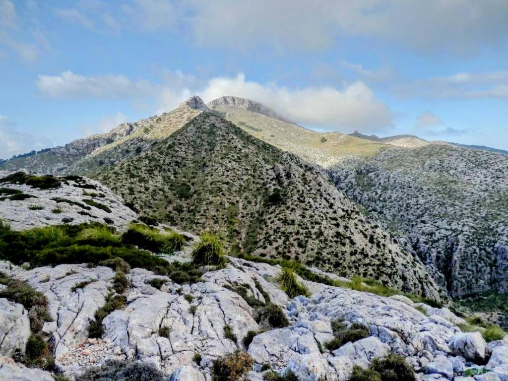 Vista panorámica del Puig Batiat y sus alrededores, mostrando montañas con vegetación, nubes y un cielo despejado.