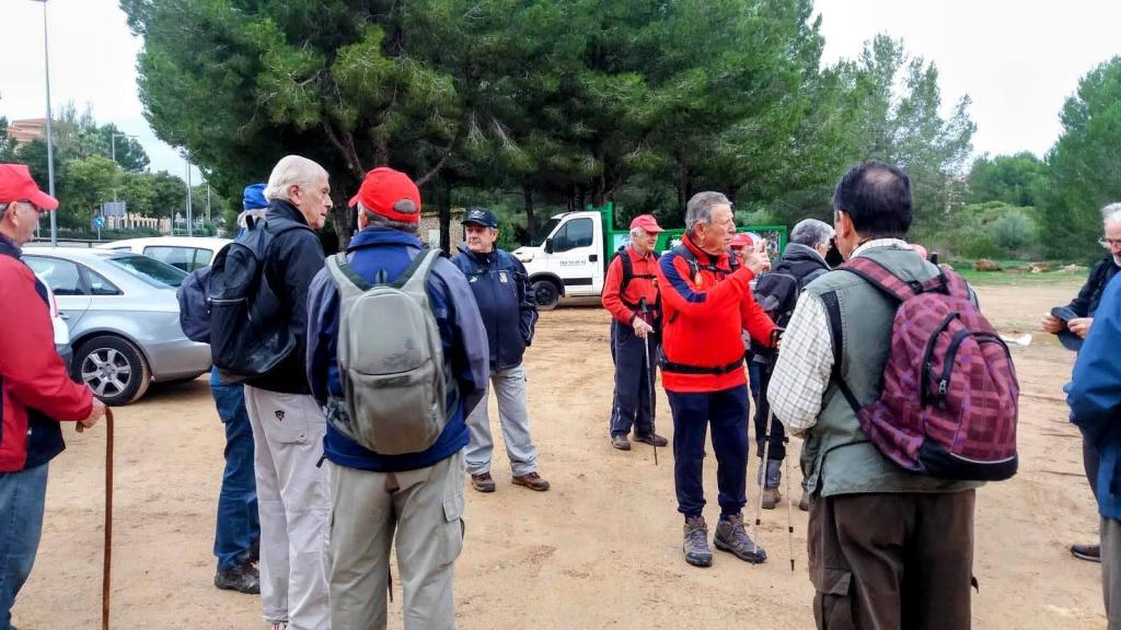 Grupo de excursionistas reunidos en un aparcamiento antes de iniciar la Ruta El Toro, con árboles y vehículos al fondo.