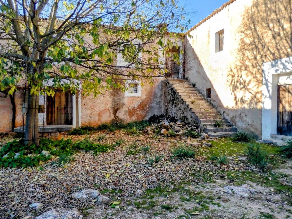 Vista de las Casas de Sa Muntanya en estado de abandono con escaleras y vegetación alrededor, en un entorno rural.