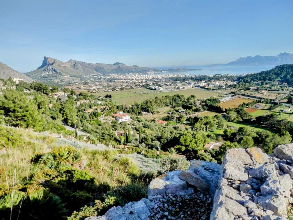 Vista panorámica del área alrededor de Puerto de Pollença, mostrando montañas y áreas agrícolas con un cielo despejado.