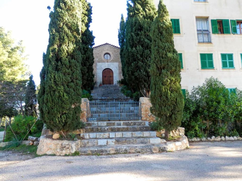 Escalera de piedras que conduce al Santuario de Santa Lucía, rodeada de cipreses y vegetación, con una edificación en el fondo.
