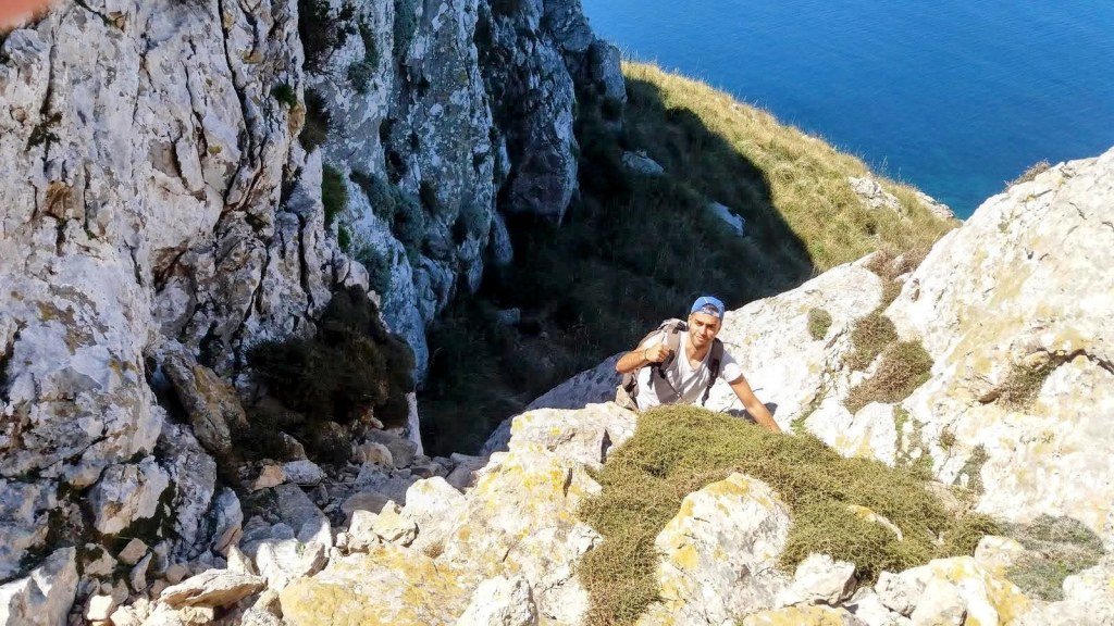 Un senderista asciende por el Pas des Torrers, con mar azul de fondo, durante la ruta hacia la Talaia Moreia.