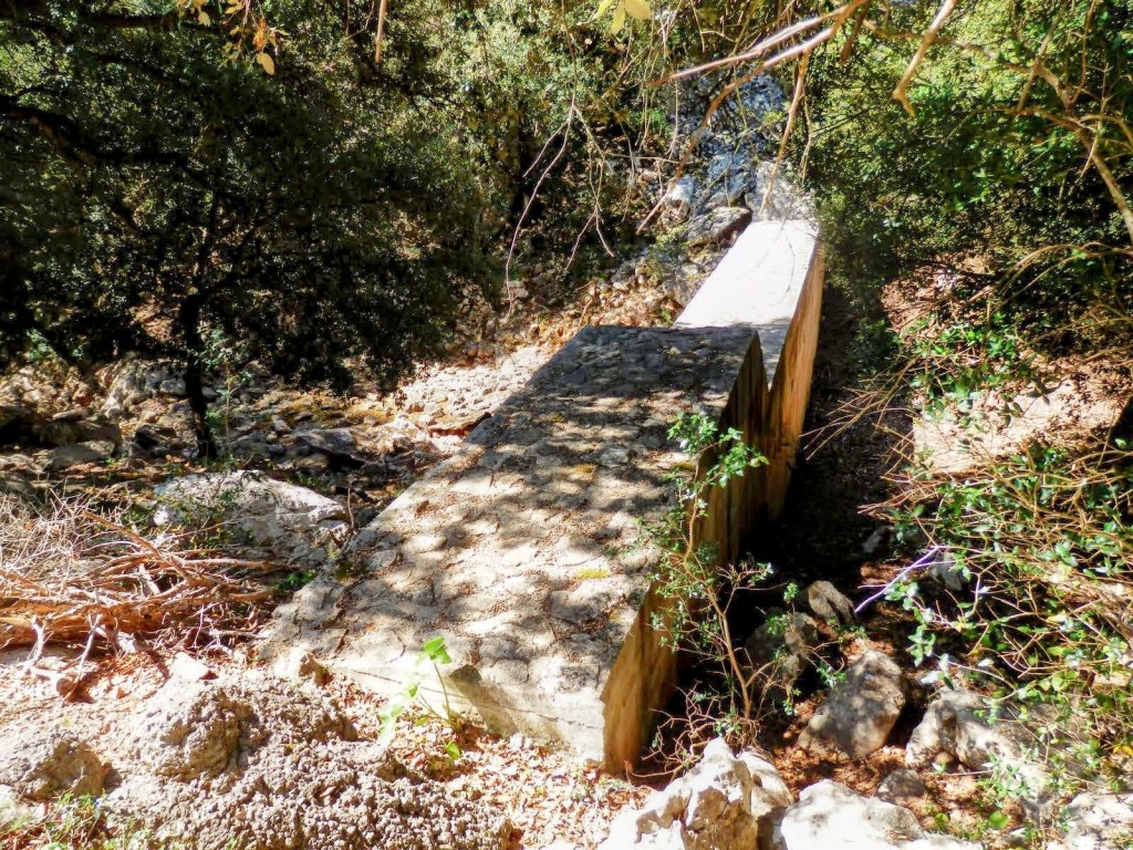 Puente de piedra natural en medio de un entorno boscoso, con vegetación densa alrededor y un lecho de río seco.