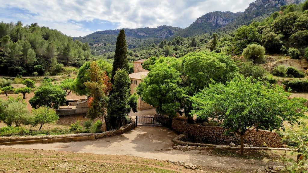 Vista del campo y la posesión de Son Malferit, rodeada de árboles y montañas en un día nublado.