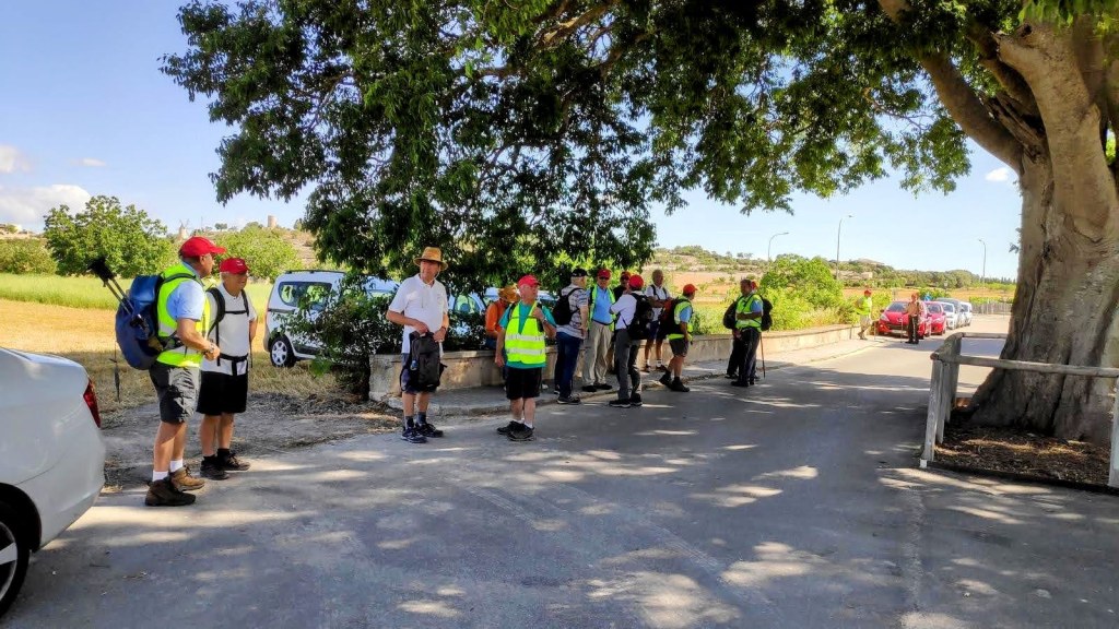 Grupo de excursionistas en el cementerio de Montuïri , con vehículos aparcados al fondo y un paisaje de campo en el horizonte.