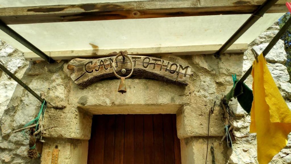 Entrada de la caseta de cazadores 'Can Tothom' con una campana y decoración rústica.