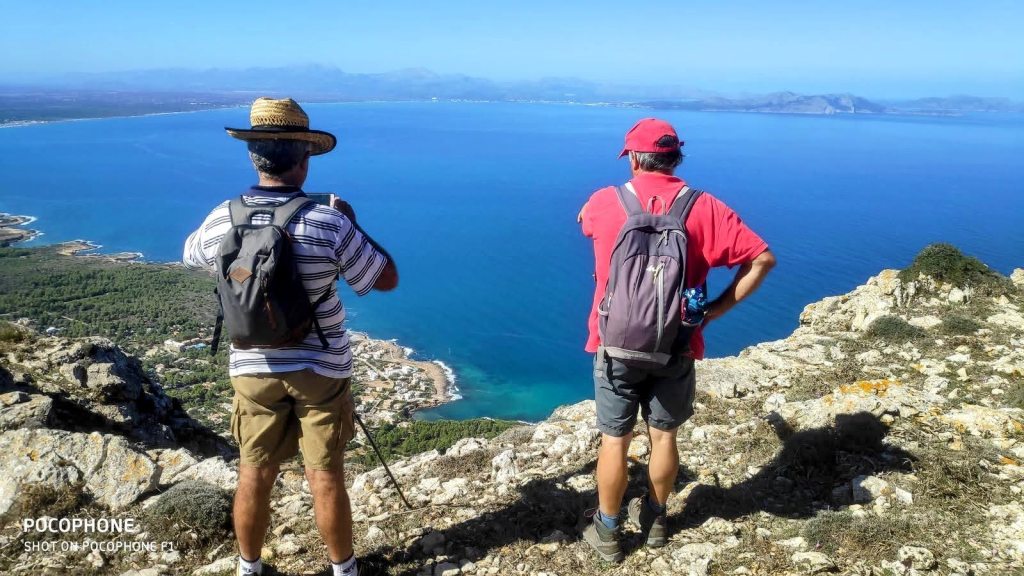 Dos senderistas contemplan el paisaje desde un mirador en la cima de la Talaia Freda, con vistas al mar y la costa.