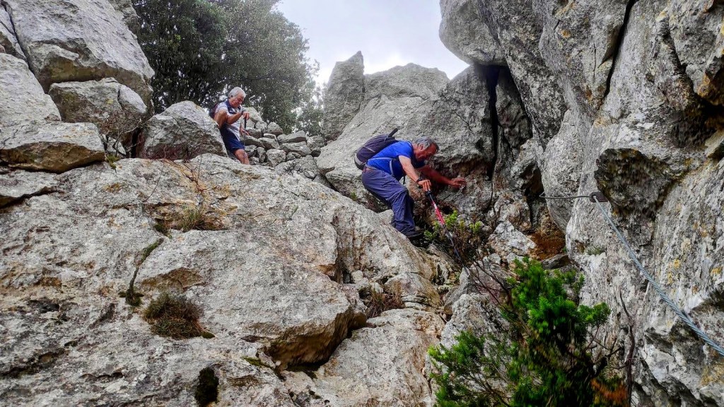 Un grupo de senderistas en el Pas d'en Bisquerra, un terreno rocoso en la Ruta Pas d’en Bisquerra. Se muestra a un hombre utilizando un cable de acero como pasamanos mientras otro lo observa.