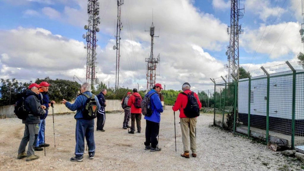 Grupo de senderistas de pie en una explanada junto a antenas repetidoras de Calviá, bajo un cielo nublado.