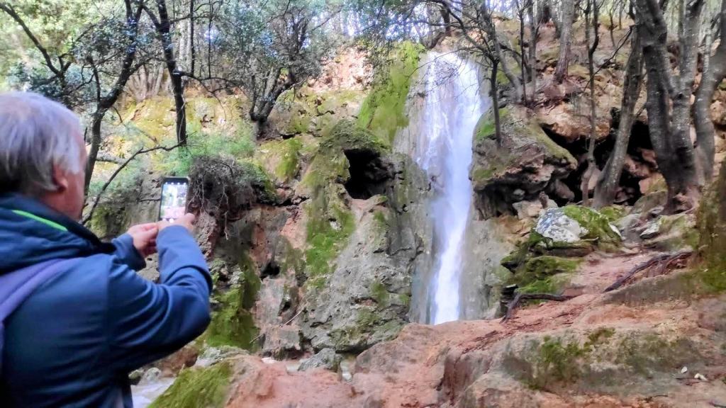 Un hombre tomando una fotografía del Salt des Freu en un entorno natural con rocas y árboles alrededor.