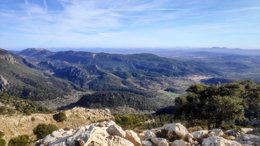 Vista panorámica desde la cima del Puig de Sa Font, mostrando un paisaje montañoso, valles verdes y un cielo despejado, ideal para ilustrar la belleza natural de la Serra de Tramuntana.