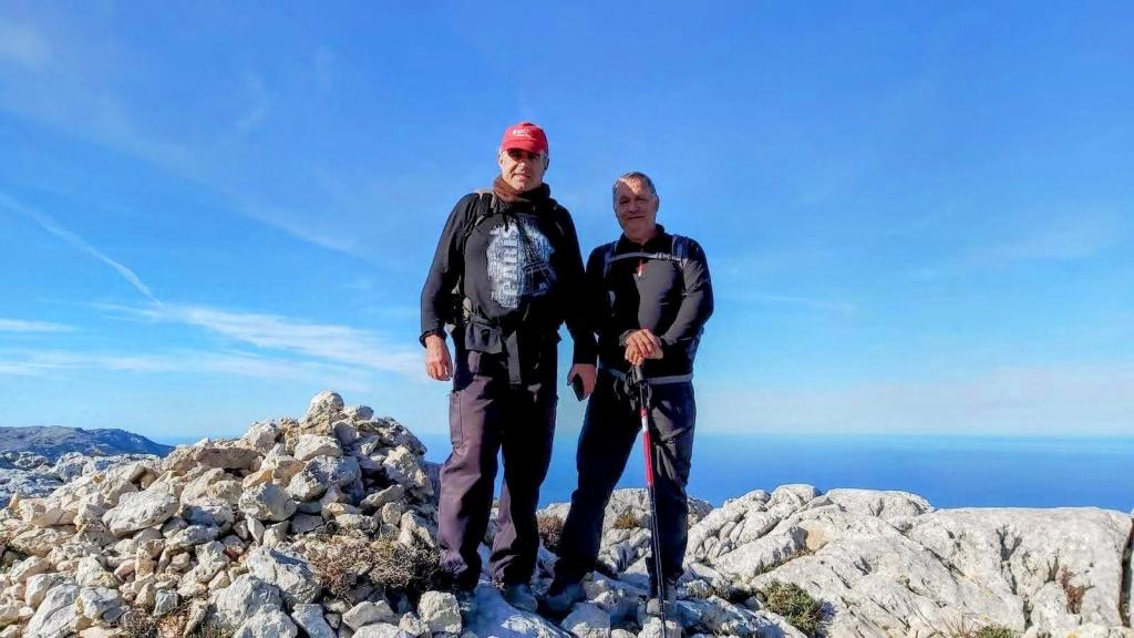 Dos personas en la cima del Es Cornador, rodeadas de rocas. El cielo es claro y azul, y se puede ver el mar en la distancia.
