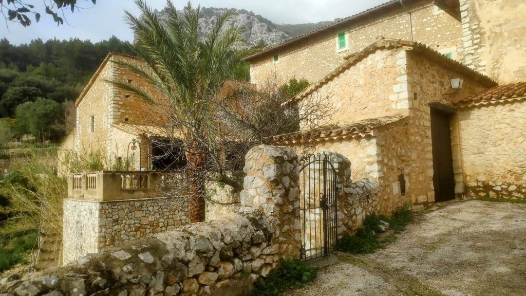 Vista de las casas de Son Alcadena en un entorno natural, con vegetación verde y montañas al fondo.