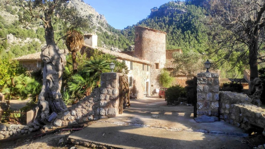 Entrada a la finca de Balitx d'Avall, con un camino de piedra y una torre de defensa visible entre la vegetación montañosa.