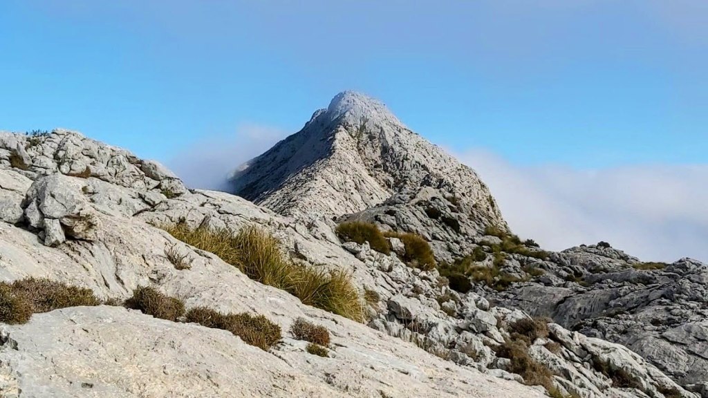 Vista de la cresta del Puig de ses Vinyes, destacando las rocas y el cielo despejado con algunas nubes en el fondo.
