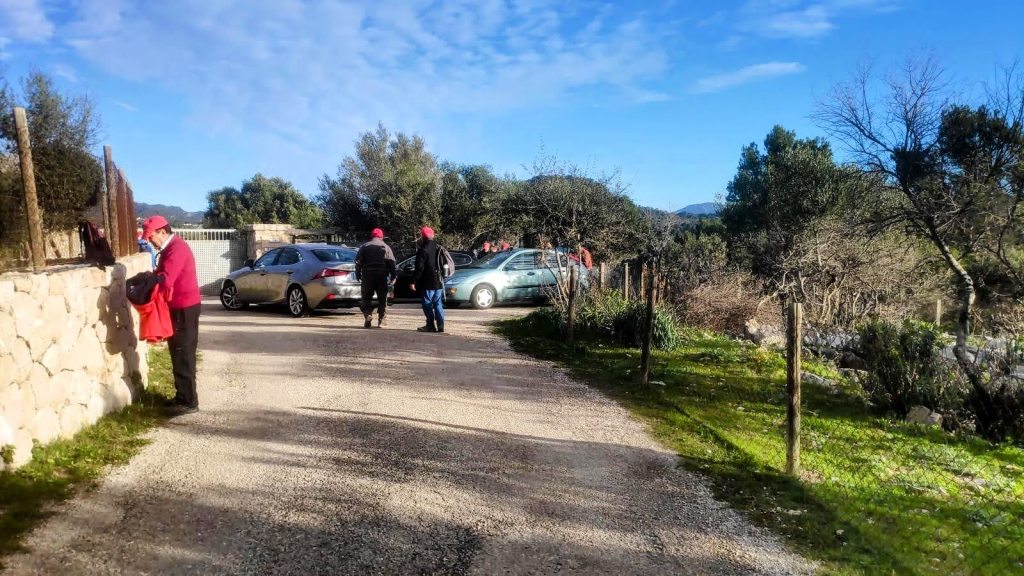 Grupo de excursionistas preparando su equipo cerca del inicio de la Ruta del Puig de Na Bauçana, con coches aparcados y un paisaje natural alrededor.