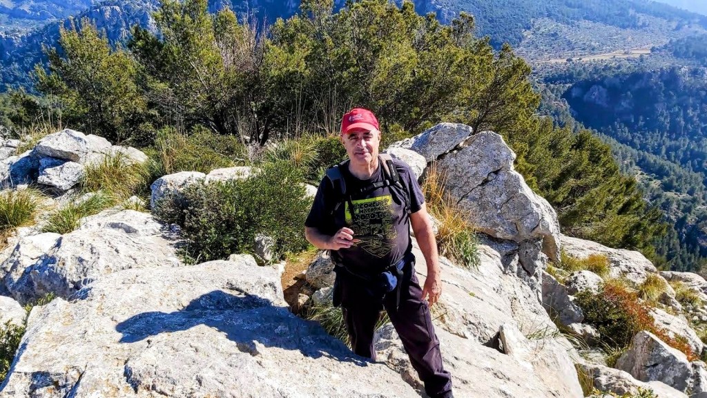 Hombre de pie sobre una roca en el Pas d’en Barona, con un paisaje montañoso, con vegetación y montañas al fondo.