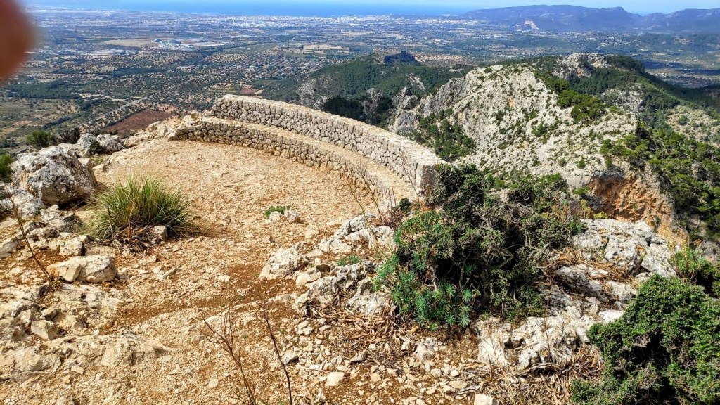 Vista panorámica desde la cima del Puig de Sa Gubia, con un mirador de piedra y paisaje montañoso al fondo, mostrando la vegetación y el valle.