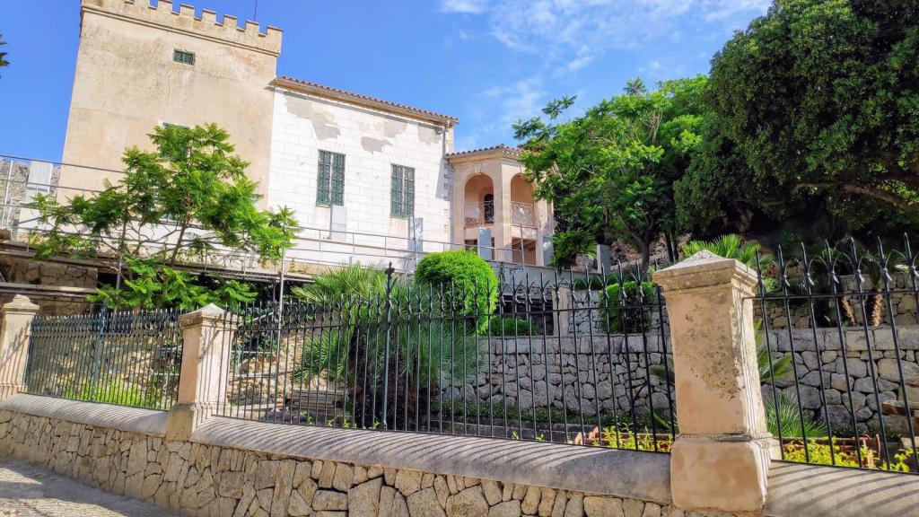 Vista de las Casas de Bòquer con una torre en la sierra de Albercutx, rodeada de vegetación y un jardín bien cuidado, con un muro de piedra y una reja al frente.