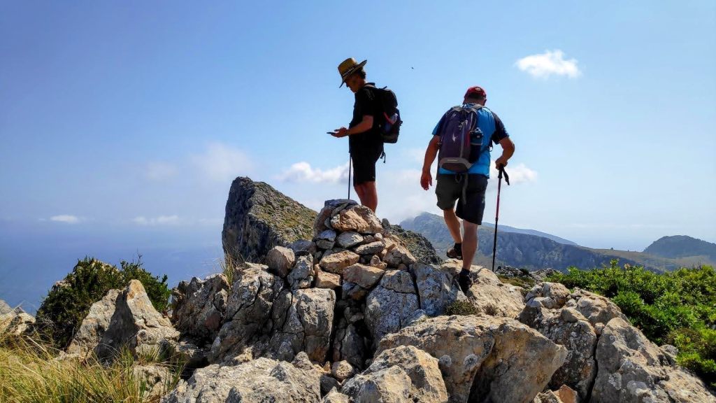 Dos senderistas en la cima del Penyal Roig ,cima rocosa en la Sierra de Albercutx, con un paisaje montañoso y un cielo despejado de fondo.